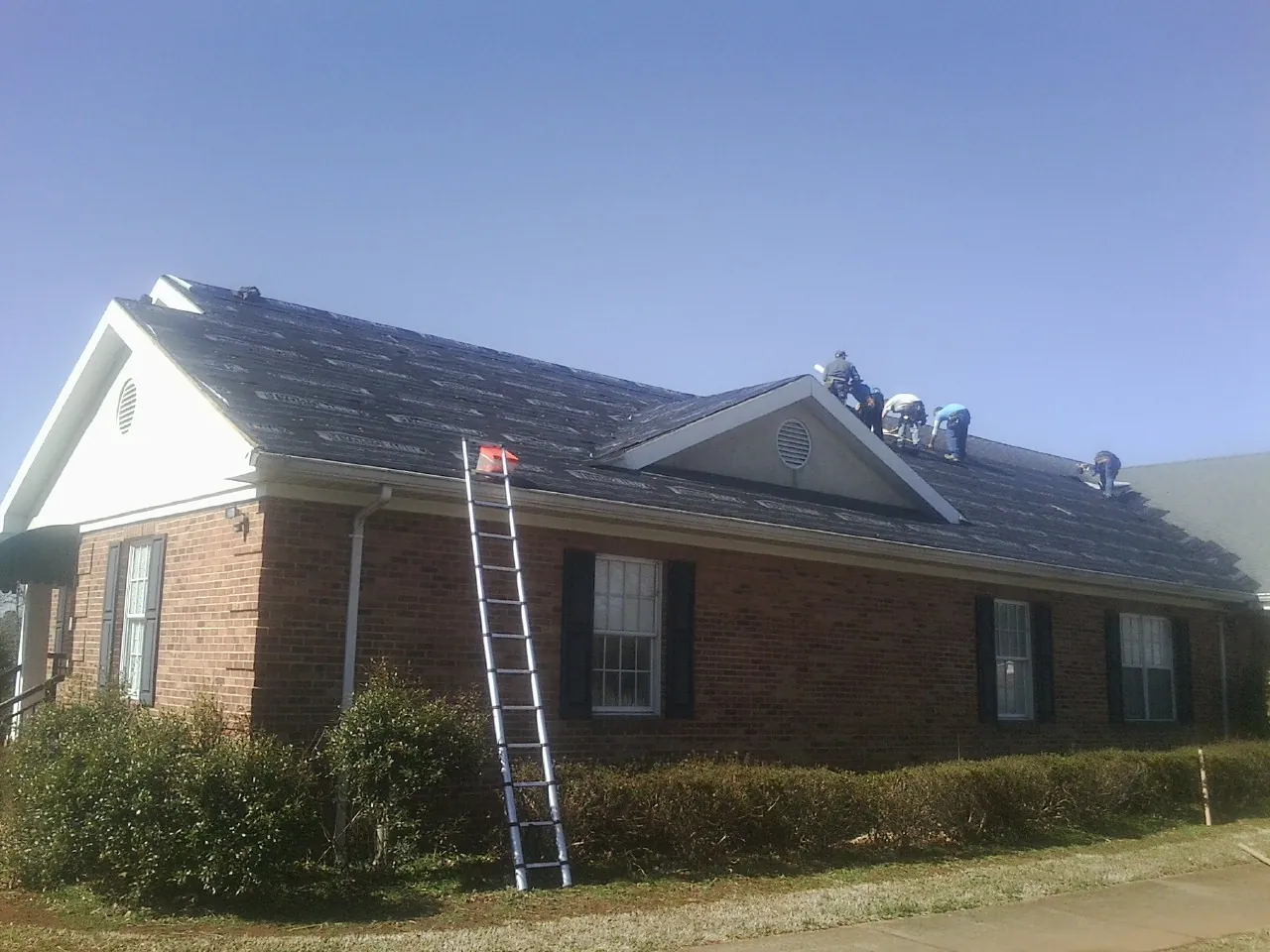 Crew tearing shingles off a brick ranch roof with a ladder set — Emergency Roof Repair work by our crew in South Whitley
