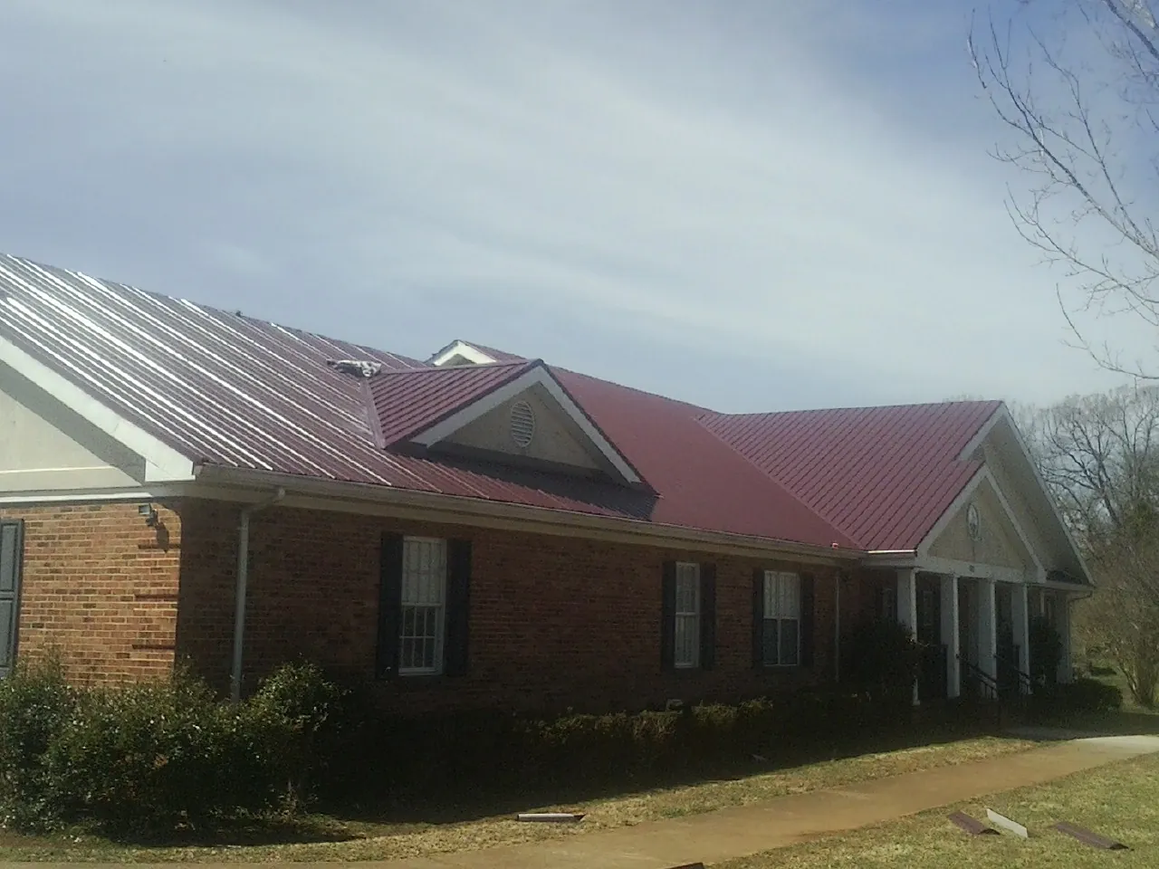 Red metal roof with gabled entries on a long brick building, from a Hail Damage Roof Repair job in South Whitley