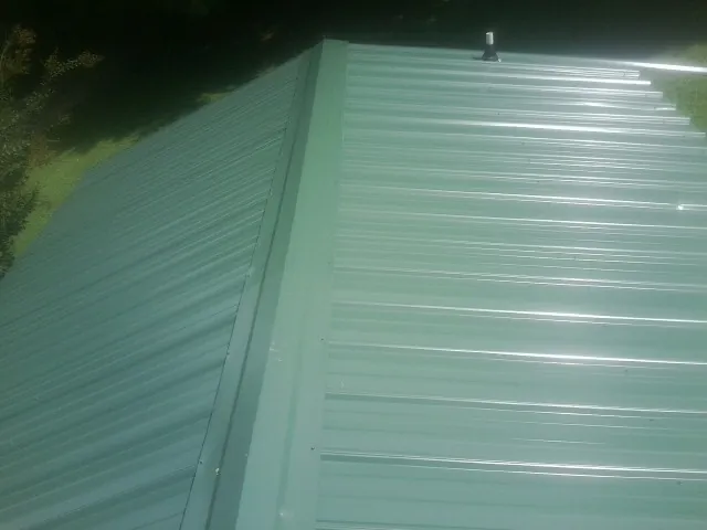 New green metal panels meeting at the ridge of a roof — Flat Roof Repair work by our crew in South Whitley