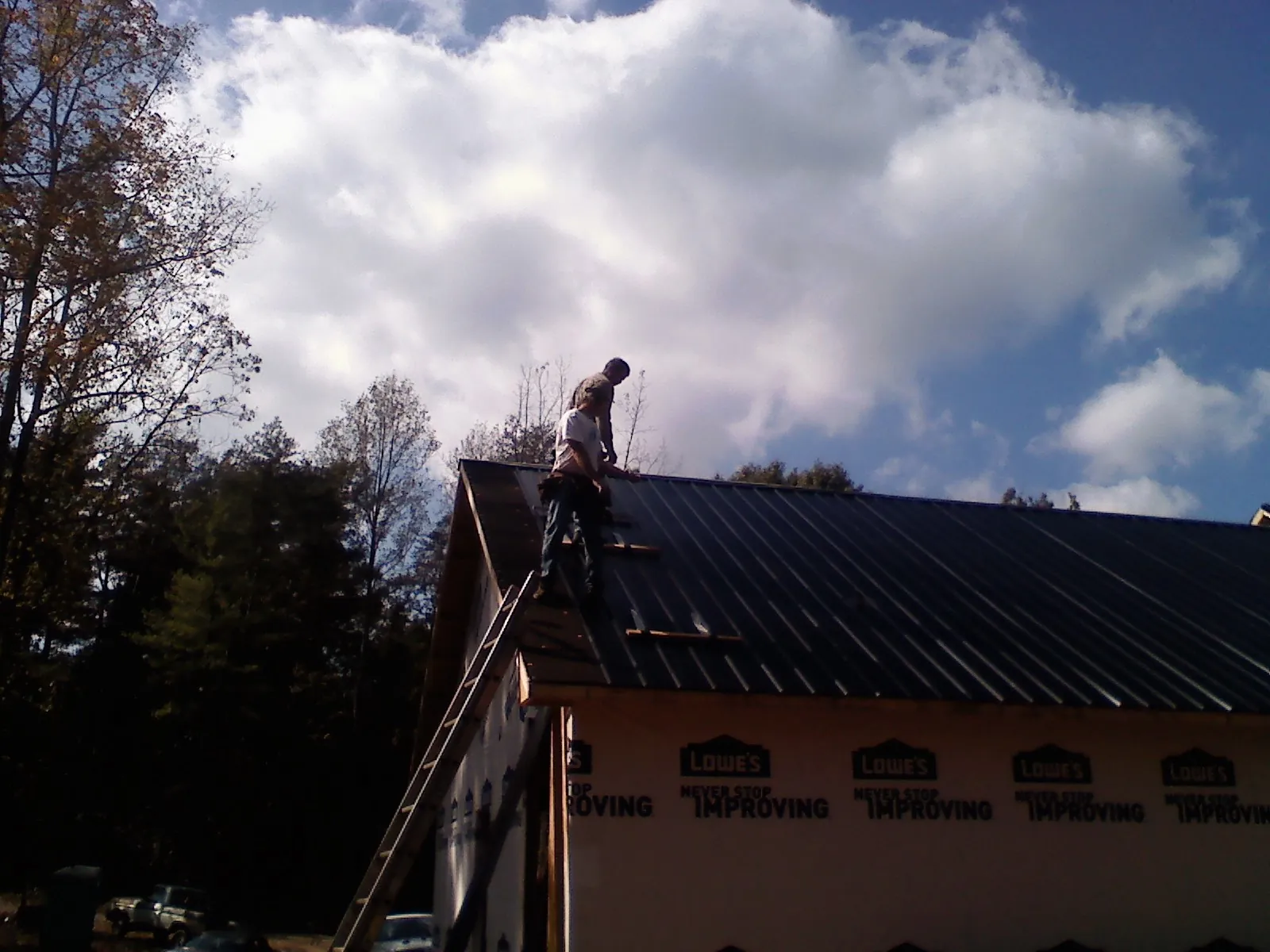 Roofer fastening dark metal panels high against a cloudy sky, from a Roof Inspection job in South Whitley