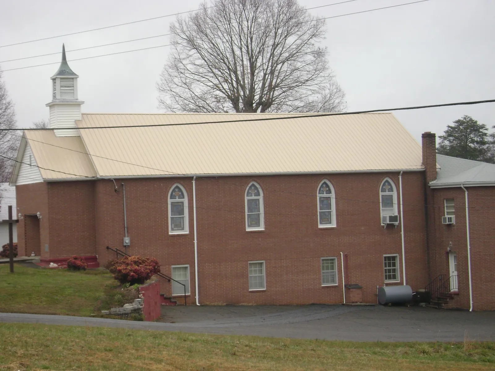 New tan metal roof on a brick church with a white steeple in South Whitley