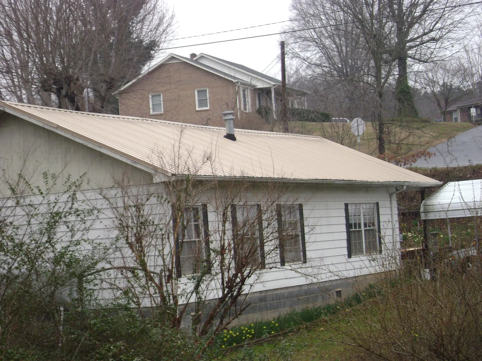 Tan metal roof on a white sided house set into a hillside — Commercial Roofing by Roofing Brothers in South Whitley